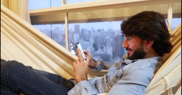 Jongeman Met Behulp Van Een Smartphone Liggend Een Hangmat Thuis — Stockvideo