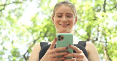 Gündüz vakti yeşil parklı akıllı telefon kullanan genç bir kadın. Yüksek kaliteli video. Cep telefonu, teknoloji, şehir kavramı.