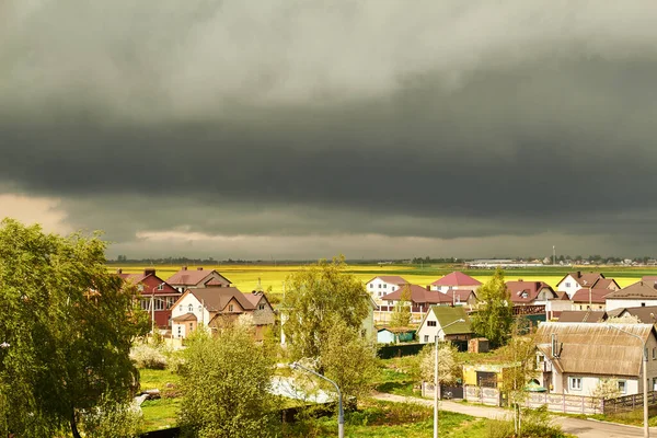 Parlak güneş ışığı altında, yağmurla dolu bulutlar ve ılık bir bahar günüyle kaplanmış karanlık gökyüzüne karşı yerleşik binalar.