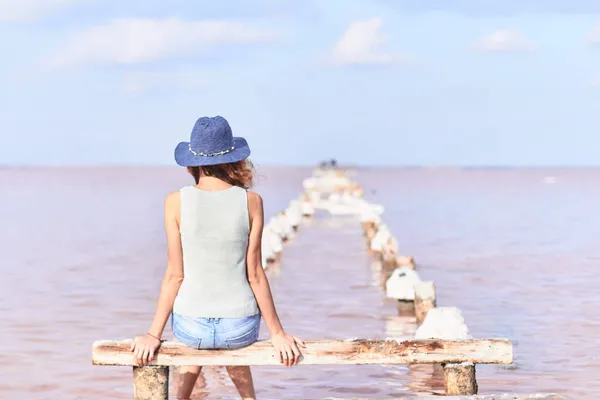 Ayakları eski bir rıhtımın kalıntılarında sallanan bir kız iyileştirici bir çamur gölünün sihirli pembe suyunun arasında uzanıyor.