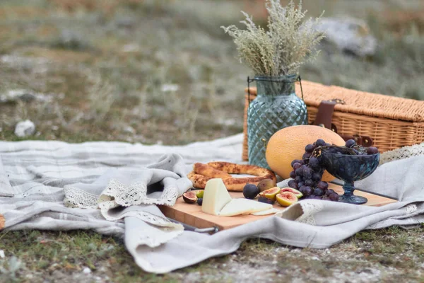 Yaz pikniğinde, meyve, ekmek ve çayır çiçekleriyle dolu bir vazoda, solmuş bozkır otlarının arka planında...