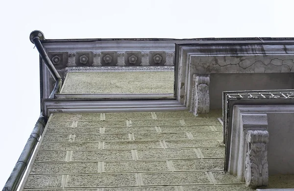 Bulutlu bir kış gökyüzüne karşı, Cornice ve dekoratif alçı duvarlar üzerinde gül şeklinde sıva süslemeli bir binanın ön cephesi.