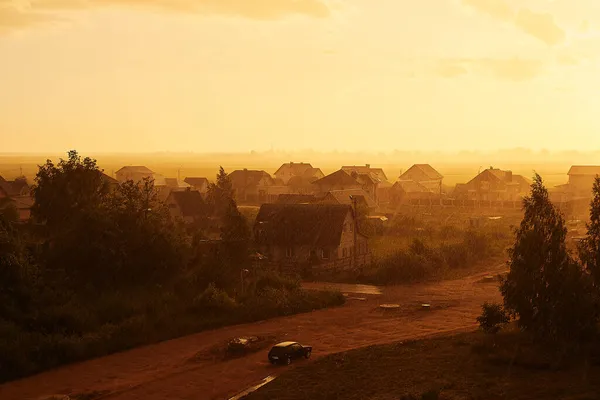 Taşra yolunda bir araba, sağanak yağış altında giden yaz günbatımının altın renklerinde.