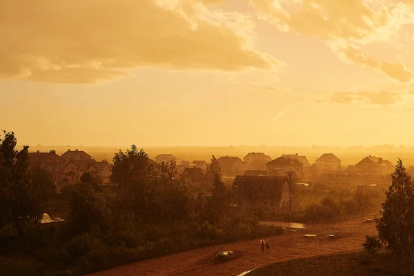 Geçen yaz gününün altın rengi ile çevrili sağanak yağmurda yürüyen insanlar.