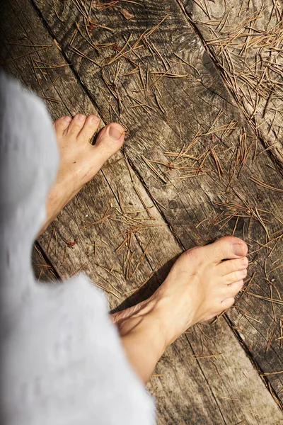 Çıplak kadın bacaklarının üst görüntüsü, eski ahşap zeminin arka planında desenli, hafifçe düşmüş çam iğneleriyle tozlanmış.