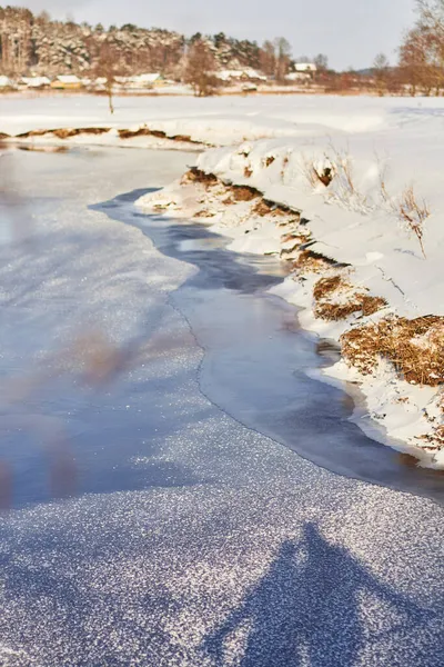 Köprüde duran bir çift aşığın gölgesi, güneşli bir kış gününde, donmuş bir kış nehrinin parlak, pırıl pırıl, buzlu yüzeyine yansıyor.