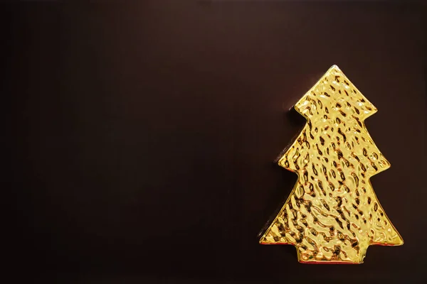 Altın ağaç şeklinde bir Noel oyuncağı, koyu kahverengi arka planda.
