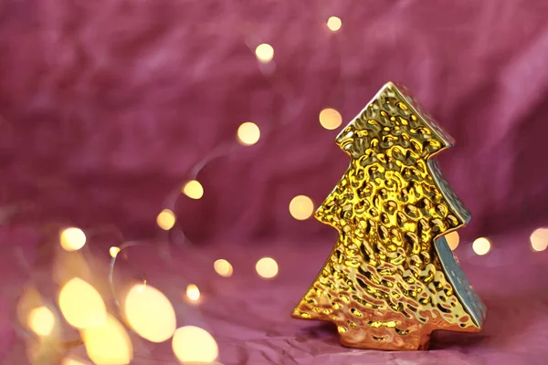 Pembe arka planda, parlak sihirli ışıkları olan altın bir Noel ağacı şeklinde Noel oyuncağı.