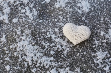 Hafif karla kaplı yüzeyin arka planında açık renkli ipliklerden yapılmış bir kalp.