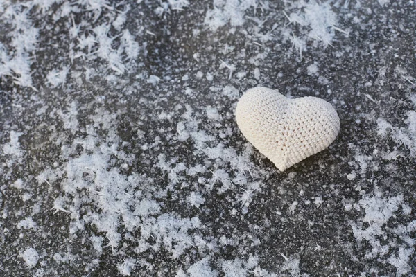 Hafif karla kaplı yüzeyin arka planında açık renkli ipliklerden yapılmış bir kalp.