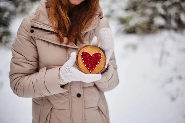 El yapımı kalp, kırmızı ipliklerle işlenmiş, bir ağaç dalının ahşap bir tabanı üzerinde, beyaz eldivenler giymiş, kadınların elinde.