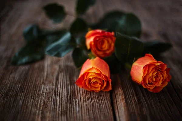 Ahşap bir yüzeyde, anlamlı bir dokusu olan bir buket turuncu gül. Bulanık odaklı arkaplan