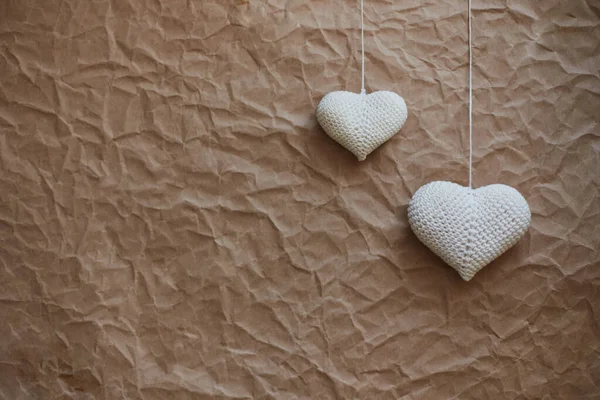 Kırışmış kağıdın dokusuna sahip açık kahverengi arkaplan üzerinde asılı beyaz örülmüş kalplerin şenlikli bileşimi