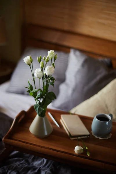 Kompozisyon, portatif bir tabloya monte edilmiş, bir buket beyaz Eustoma, küçük bir vazonun içinde duruyor, bir fincan ve bir kalem ile bir defter, yatak odasının akşam alacakaranlığı ile çevrili