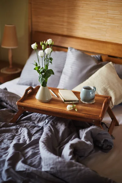 Portatif bir yatağa monte edilmiş, küçük bir vazoda bir buket beyaz Eustoma, bir fincan ve bir kalem ile bir not defteri, akşam kalemi ile çevrili, bir parça parçalanmış bir yatak.