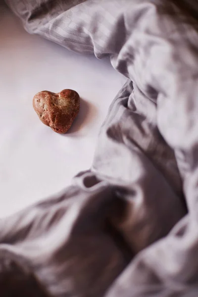 Küçük taş bir kalp, insan yapımı bir doğa, bulanık bir arka planda hafif buruşuk mor bir battaniye ile çevrili