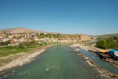 Waters of the Tigris river as it passes through the city of Hasankeyf with a cliff full of caves in an area of Mesopotamia clipart