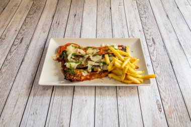 Pesto soslu, patatesli, domatesli ve yanında patates kızartması olan Parmesan peynirli Akdeniz şnitzeli.