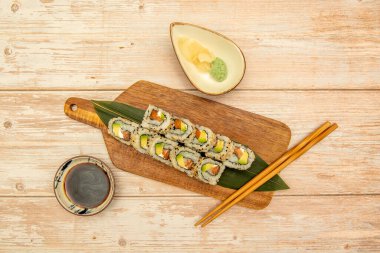 Uramaki California suşisinin en iyi görüntüsü susam tohumlu suşi, Norveç yosunu, krem peynir, somon balığı ve olgun avokado wasabi, soya sosu ve ahşap çubuklarla.