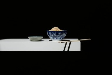 Beyaz rafta soya sosu ve çubuklu mavi kase beyaz pirinç.