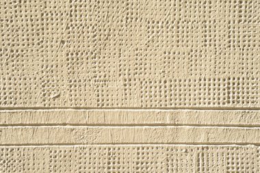 Bir binanın ön cephesinin dokusu, birden fazla çizgi ve krem rengi ile boyanmış delikler.