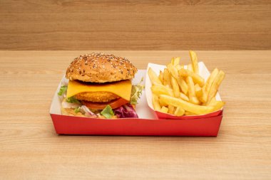 Çedar peynirli çıtır tavuk burger, domates ve marul, mayonez ve ketçap, hafif ahşap tezgahta patates kızartması.