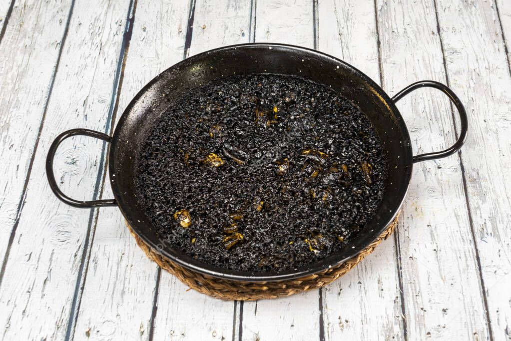 Black rice paella with squid on a black paella pan on a white table