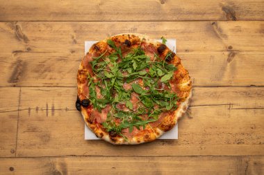 İspanyol jambonu ve roka ile ince hamurlu Serrana pizzası taş fırında pişirilir ve ahşap bir masada sunulur.