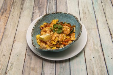 Pad Thai, pirinç eriştesi, balık sosu, tamarind ezmesi, kırmızı biber, fasulye lahanası, karides, fıstık ezmeli tavuk ve kişniş, limon dilimi, muz çiçeği, palmiye şekeri ve kızarmış kırmızı biber.