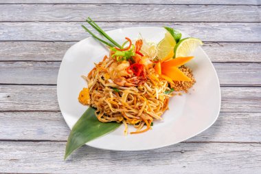 Pad Thai, pirinç eriştesi, balık sosu, tamarind ezmesi, kırmızı biber, fasulye lahanası, karides, fıstık ezmeli tavuk ve kişniş, limon dilimi, muz çiçeği, palmiye şekeri ve kızarmış kırmızı biber.