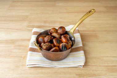 Klasik metal tencere dolusu kavrulmuş kestane tipik İspanyol sonbaharı ve kışı ahşap bir masada geçirir.