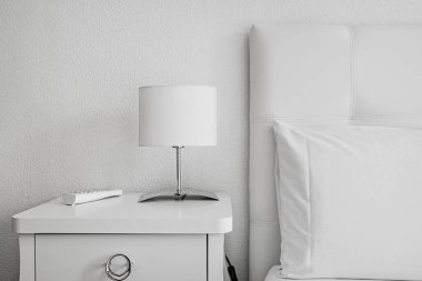 Kiralık bir dairede beyaz deri döşeme, beyaz laktuvar komodin ve lamba.