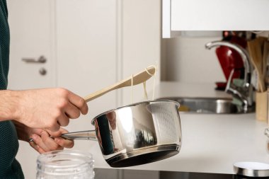 Paslanmaz çelik bir tavada spagetti pişiren adam onları tahta bir kaşıkla karıştırıyor.