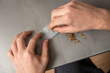 Yetişkin bir adamın elleri rulo kağıdı özel bir tütün karışımıyla sarıp sonra tüttürür.