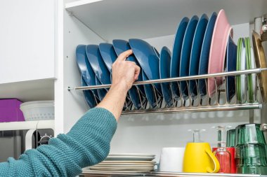 Bir adamın eli mutfak dolabının drenajına mavi tabak koyuyor.
