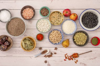 Ham ürünlerle dolu farklı ve güzel kaseler. Biber çekirdeği, siyah fasulye, kahverengi mercimek, defne yaprağı, kaşıkta kırmızı biber, maydanoz, beyaz ahşap masada elma ve armut.