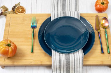 Mavi tabaklar, yanardöner çatal bıçak seti ve bambu masasında pembe domatesler.