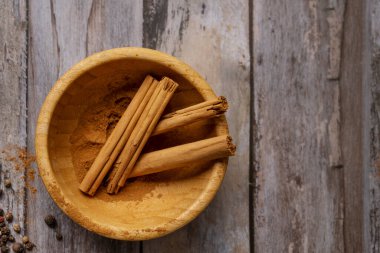 Bambu ahşap kase, tarçın çubukları ve eski ahşap masa üzerinde tarçın.
