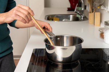 Seramik hob üzerinde spagetti sosu karıştıran genç bir adamın elleri.