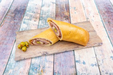 Pişmiş jambonla doldurulmuş Venezuela ekmeği, taze peynir ve ahşap masada biberli zeytin.