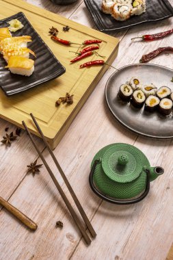 Yeşil çay demliği, ahşap yemek çubukları, somon balığı, maki suşi, nigiri, kırmızı acı biber, yıldız anason ve bambu tahtasıyla sakin bir hayat.