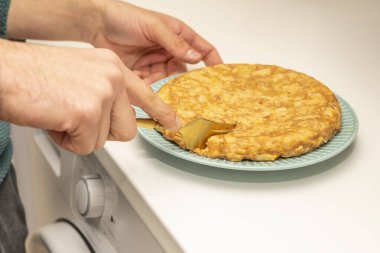 Mavi tabakta altın kaplama patates omleti ve beyaz mutfak tezgahı.