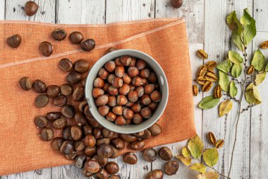 Tahta masaya dağılmış bir kase fındık ve mevsimlik kestane.