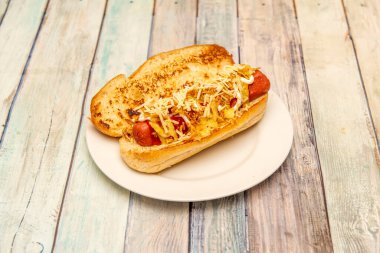 Sosisli, hardallı, rendelenmiş peynirli, ketçaplı ve beyaz tabakta mayonezli Brioche ekmeği.