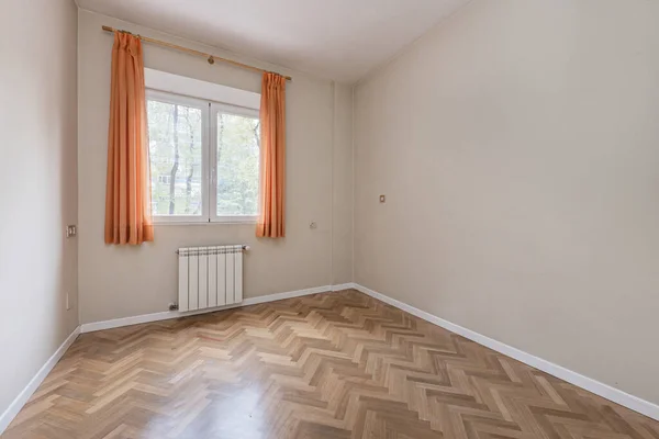 Empty bedroom with orange curtains window and herringbone-shaped parquet