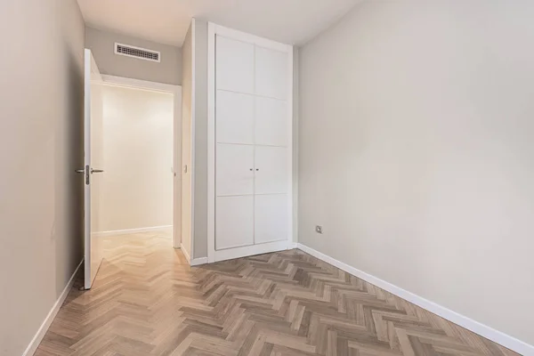 Empty bedroom with white door, built-in wardrobes, herringbone parquet and ducted air conditioning
