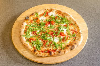 Burrata peynirli pizza, vişneli domates, roka ve taş fırında pişirilmiş serano jambonu.