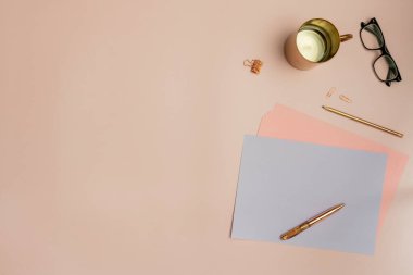Pastel pembe tonlarda kağıt, kırmızı altın kalemler, kalemler ve okuma gözlükleriyle.