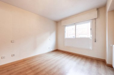 Empty room with a large window through which light enters in abundance with the walls painted in cream color