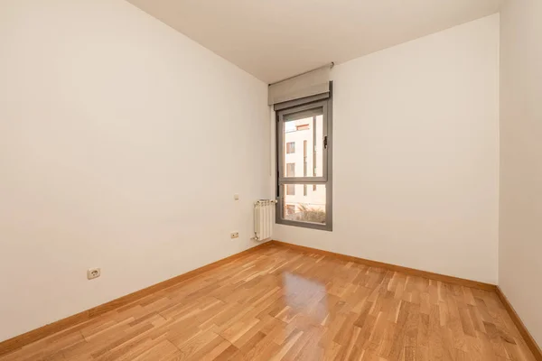 Empty apartment room with window, aluminum radiators and oak parquet flooring